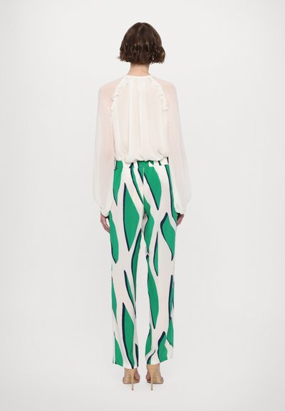 Blouse blanche transparente avec détails à volants, associée à un pantalon à jambes larges présentant un motif de feuilles vertes et bleu marine sur fond blanc.