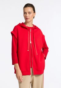 Rode zip-up hoodie met een trekkoordkap, korte mouwen en ribgebreide boorden. Gemaakt van een zachte stof met een effen kleurafwerking.