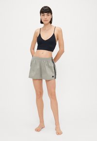 Crna sportska grudnjak s tankim trakama, u kombinaciji sa svijetlo sivim šortsevima s crnim bočnim trakama i elastičnim pojasom.