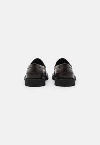 Mocassins en cuir noir avec une finition lisse, présentant un bout arrondi et une semelle en caoutchouc épaisse et texturée. Accents de double couture sur le dessus.