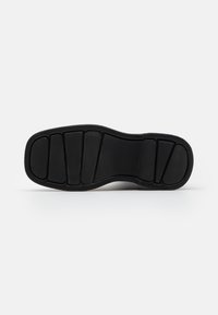 Semelle de chaussure en caoutchouc noir, présentant un design texturé avec des sections segmentées pour l'adhérence et la flexibilité. Forme plate et arrondie sans talon.