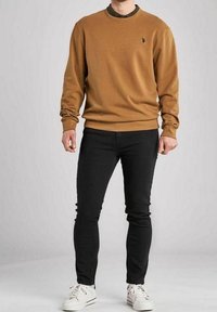 Brun sweatshirt med rund hals och ribbade ärmslut, kombinerad med svarta skinny jeans och vita sneakers. Har en liten logotyp på bröstet.