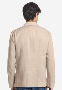 Beige linnblazer med rak skärning, en bakslits och långa ärmar. Slät textur och minimala sömnadsdetaljer.