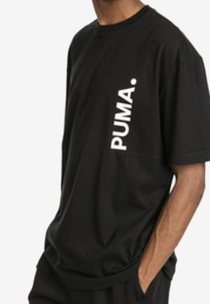 Mężczyzna noszący czarną koszulkę z krótkim rękawem z pionowo nadrukowanym na białym słowem "PUMA." po lewej stronie klatki piersiowej.