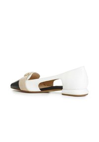 Chaussure plate bicolore avec un bout pointu noir, des panneaux beiges et blancs, un design ouvert sur les côtés et un petit talon.