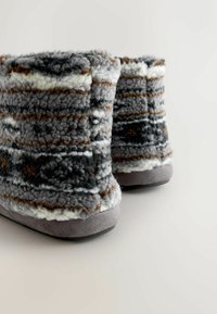 Vlezige grijze en bruine enkellaarsjes met witte accenten. Zachte, gemêleerde bovenkant en een stevige grijze zool. Rondige vorm met een gezellige uitstraling.