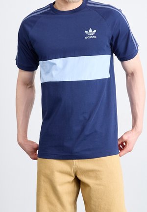 T-shirt bleu marine avec une rayure horizontale bleu clair, encolure ronde, manches raglan courtes, et logo blanc Adidas sur la poitrine.