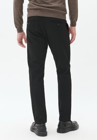 Pantalones negros ajustados, con dos bolsillos traseros con botones y una textura suave. Combinados con zapatos negros y un suéter marrón.