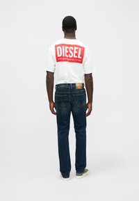 Camiseta blanca de manga corta con el logo rojo de "DIESEL", combinada con jeans de mezclilla azul oscuro, con un corte recto clásico y detalles de costura sutil.