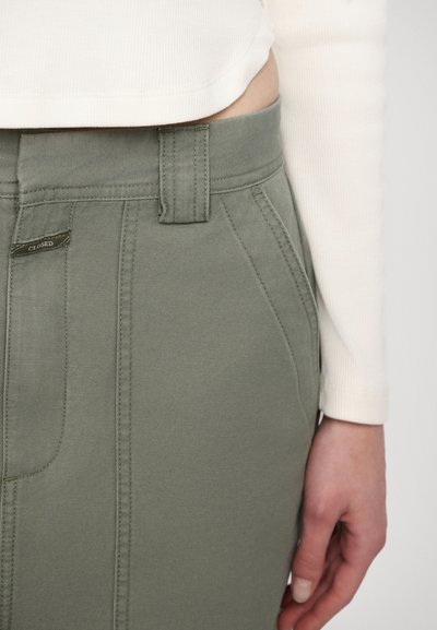 Pantalons ajustés verts avec un design structuré, dotés d'une taille et de poches latérales. Le tissu semble robuste avec des coutures visibles.
