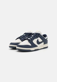 Navy and white leather sneakers with perforated toe, round laces, and a textured rubber sole. Features a prominent Nike logo in navy.