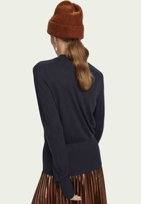 Granatowy sweter z ribbowym dołem i mankietami, noszony z metaliczną spódnicą plisowaną. Ceglany, dziany beret dodaje faktury do stroju.