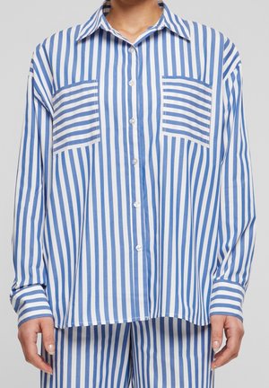 Niebiesko-biała koszula z pionowymi paskami zapinana na guziki, z dwoma poziomymi kieszeniami na piersi, noszona z pasującymi spodniami w paski.