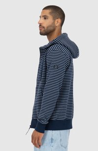 Felpa a strisce blu navy con zip frontale, cappuccio regolabile con cordino e polsini a costine. Presenta un logo ricamato sulla manica sinistra.