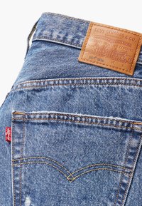 Jeans de mezclilla azul con una etiqueta de cuero marrón claro con texto en relieve, una etiqueta roja de Levi's en el bolsillo y patrones de costura clásicos.