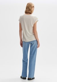 Haut court à manches roulées beige clair, associé à un jean droit taille haute bleu et des sandales noires. Style simple et décontracté.