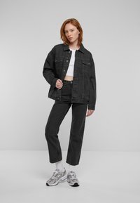 Zwarte spijkerjack met twee borstzakken, gestyled met een kort wit T-shirt, zwarte jeans en grijze sport schoenen.