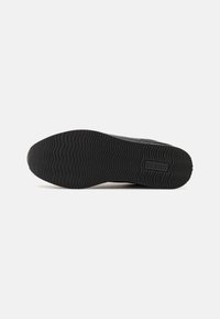Semelle de sneaker en caoutchouc noire avec un motif texturé et ondulé ; possède le logo de la marque imprimé au centre.