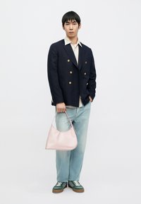 Námořnický dvouřadý blejzr, pruhované tričko, světle modré džíny, zelené tenisky. Drží světle růžovou lesklou kabelku se zaobleným tvarem.