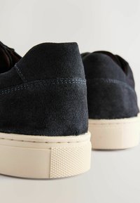 Blaue Wildlederschuhe mit einer cremefarbenen Gummisohle. Verfügt über eine glatte Textur und kontrastierende Nähte entlang der Kanten. Minimalistisches Design.