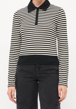 Haut à manches longues rayé horizontalement noir et blanc avec col noir et patte de boutonnage, associé à un pantalon noir.