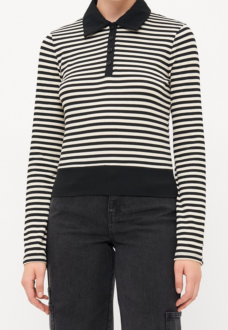 Haut à manches longues rayé horizontalement noir et blanc avec col noir et patte de boutonnage, associé à un pantalon noir.