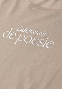 Beige stof met witte bedrukte tekst "Laboratoire de poésie" in een elegant schreeflettertype.