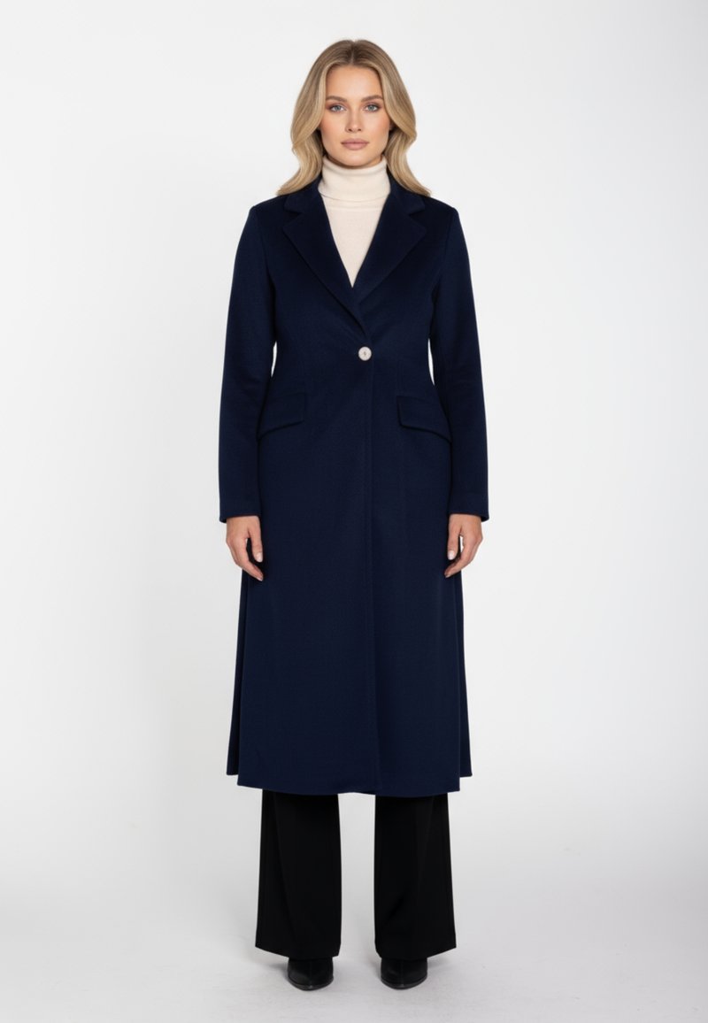 Marineblauer Mantel aus Wollmischung mit langem Schnitt, Revers mit Kerbspitze, Ein-Knopf-Verschluss und zwei vorderen Taschen. Getragen über einem beigen Rollkragenpullover.