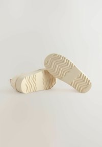 Zapatos de plataforma blancos con suelas de goma texturizadas y patrón en zigzag. La parte superior presenta un material suave y trenzado. Diseño limpio, sin hardware visible.