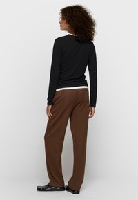 Top negro de manga larga sobre una camisa blanca, combinada con pantalones marrones de pierna ancha. Los pantalones tienen un bolsillo trasero y una textura suave.