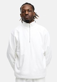 Weißer Viertelreißverschluss-Pullover aus weichem Stoff, mit hohem Kragen und Raglanärmeln, glatter Textur und minimalistischem Design.