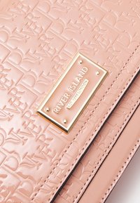 Rosaskimrande konstläderhandväska med en präglad design. Har en guldfärgad platta med "RIVER ISLAND" och dekorativa nitar.