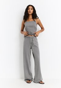 Graue Denim-Weite-Hosen mit gebundenem Bund, kombiniert mit einem passenden, kurzen Tanktop. Glatte Textur, minimalistisches Design und neutrale Farbe.