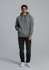 Szary kaptur z kieszenią z przodu i sznurkami, w połączeniu z ciemnymi dżinsami i białymi tenisówkami. Gładka tekstura, casualowy design.