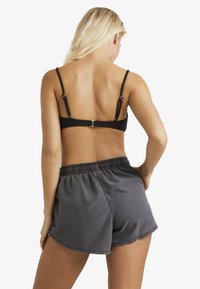 Must mustriba bikiin üst, reguleeritavate rihmade ja kuldsete detailidega, millele on lisatud hallid tekstuuriga lühikesed püksid elastse vöökoha jaotusega.