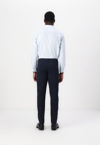 Ljusblå långärmad skjorta med knappmanschetter, bärs med marinblå byxor, visar en slim fit och en slät textur. Svarta skor fulländar looken.