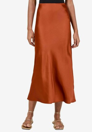 Jupe midi en satin couleur orange rouille, avec une texture lisse, une taille ajustée et une forme évasée. Associée à des sandales dorées à talons.