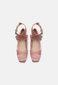 Pink satin shoes with a square toe, crisscrossed detailing, and ankle strap with buckle fastener. Smooth texture and soft, elegant design.