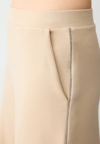 Beige stoffen joggers met een soepele textuur, elastische tailleband en een gedetailleerde grijze stiksels langs de zak.