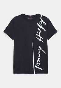 Maglietta nera in cotone con colletto rotondo, caratterizzata da un logo bianco in corsivo "Tommy Hilfiger" stampato diagonalmente sulla parte anteriore.