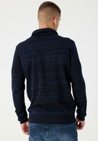 Suéter de rayas azul marino con cuello chal. Hecho de un tejido de punto suave, cuenta con puños y cintura acanalados, diseñado para un ajuste relajado.