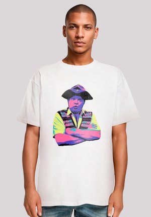 White cotton t-shirt featuring a colorful graphic of a man in a hat and vest, with crossed arms. The design is vibrant and bold.