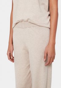 Beige Strickoberteil mit weitem Halsausschnitt und kurzen Ärmeln, kombiniert mit passenden beige weit geschnittenen Hosen. Die Textur wirkt weich und glatt.