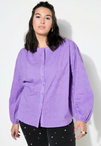 Camicia viola con maniche lunghe e a palloncino, decorata con un motivo testurizzato. Abbinata a pantaloni scuri impreziositi da perle bianche.
