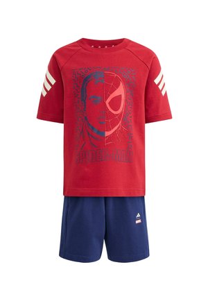 T-shirt rossa a maniche corte di Spider-Man con grafica del volto diviso e pantaloncini blu con loghi Adidas e Marvel su sfondo bianco.