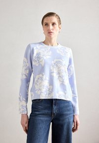 Lys blå genser med hvitt blomstermønster, ribbestrikket halskant og kant, kombinert med mørkeblå denimjeans. Myk tekstur, avslappet passform.
