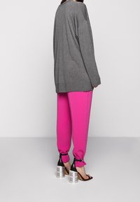 Oversized gray sweater, bright pink tapered pants with elastic cuffs, and black high-heeled sandals with silver metal accents.