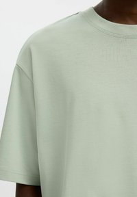 T-shirt en coton vert clair avec un col rond et des manches courtes ; texture lisse et douce avec une coupe décontractée.