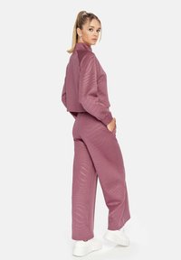 Paarse cropped jas en bijpassende wijde broek gemaakt van gestructureerde stof, met een subtiel golfpatroon en ribbelmanchetten. Witte sneakers.