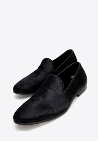 Czarne buty wsuwane z wydłużonym noskiem, pokryte miękkim, teksturowanym materiałem, z gładkim czarnym wykończeniem wewnątrz i małym obcasem.